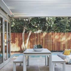 an outdoor dining area with table, bench and pool in the backround on a sunny day