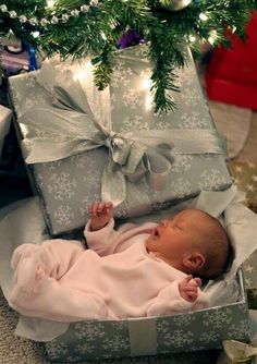 a baby laying in a box under a christmas tree