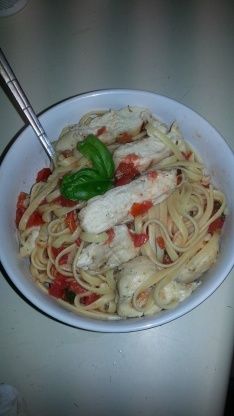 a white bowl filled with pasta and meat on top of a table next to a fork