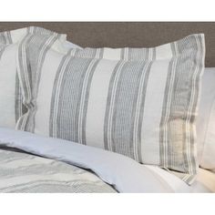 a close up of two pillows on a bed with white and gray linens in the background