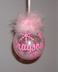 a pink ornament hanging from a wall with a fuzzy ball and name on it