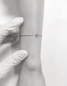 a person in white gloves is holding up a small tattoo on their left arm that has an arrow drawn across it