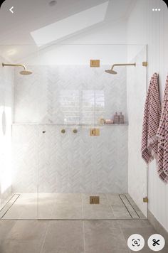 a bathroom with white tile and gold hardware on the shower door, towel racks in the corner