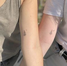 two people with matching tattoos on their arms, one holding the other's arm