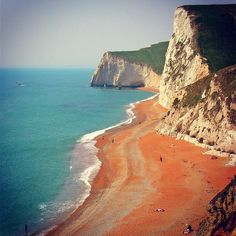 people are walking on the beach next to the ocean and cliffs that look like they have been built into the cliff