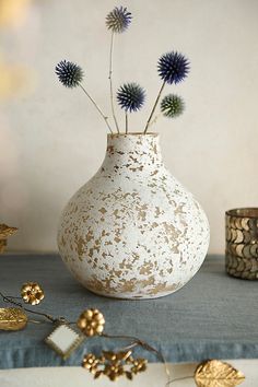 a white vase filled with purple flowers sitting on top of a blue table cloth next to other items