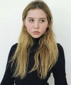 a young woman with long blonde hair and blue eyes is looking at the camera while wearing a black turtle neck sweater