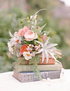 a stack of books with flowers and greenery on top