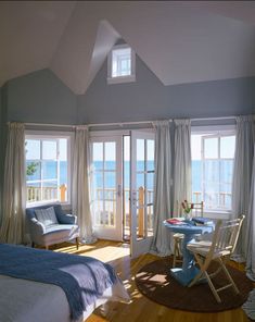 a bedroom with a bed, chairs and windows overlooking the ocean on a sunny day