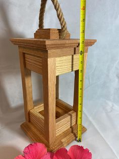 a small wooden lantern with rope hanging from it's side and pink flowers next to it