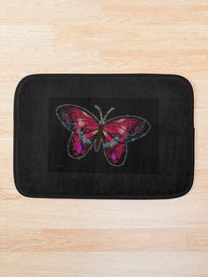 a bath mat with a pink butterfly embroidered on the front and back, sitting on top of a wooden floor