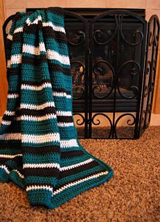 a green and white crocheted blanket sitting next to a fireplace