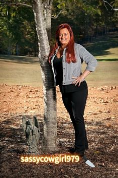 a woman standing next to a tree with her hands on her hips, posing for the camera