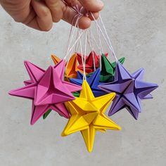 a hand is holding several origami stars in different colors and shapes, each being held by string