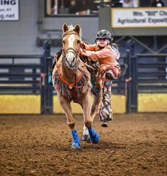 a man riding on the back of a brown horse in an indoor arena at night