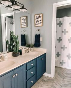 a bathroom with blue cabinets and white counter tops is pictured in this image, there are two framed pictures on the wall above the double sinks