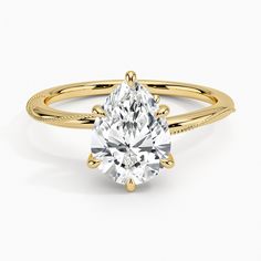 a yellow gold engagement ring with a pear shaped diamond in the center, on a white background