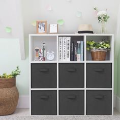 a white bookcase with black bins next to a potted plant