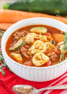 a bowl of soup with dumplings, meat and vegetables in it on a red napkin