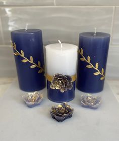 three blue candles with gold leaves on them and one white candle in the middle next to it