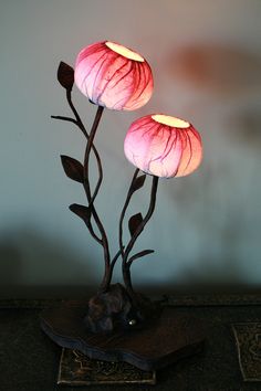 two pink flowers are lit up on a table with a black base and brown leaves