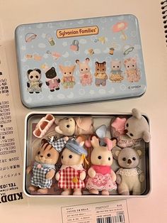 several small stuffed animals are in a tin on the table next to an open book