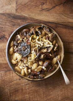 a bowl filled with pasta and mushrooms on top of a wooden table next to a spoon