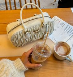 a woman holding a cup of coffee next to a handbag on a wooden table