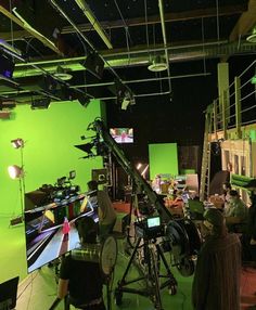 several people are sitting in front of green screen televisions and recording equipment, while one person is on the phone