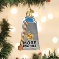 a christmas ornament hanging from a tree with lights in the background and more cowbell written on it