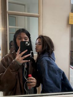 two women standing in front of a mirror looking at their cell phones