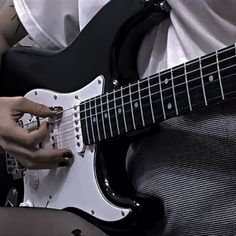 a person playing an electric guitar with their hands on the fretboard, while sitting down