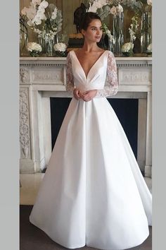 a woman standing in front of a fire place wearing a white dress with long sleeves