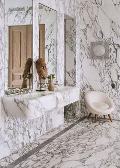 a bathroom with marble walls and flooring, including a white chair in front of the sink