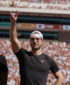 a man in black shirt and white visor waving to the crowd at a football game