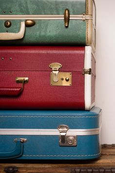 three suitcases stacked on top of each other in front of a white wall and wooden floor