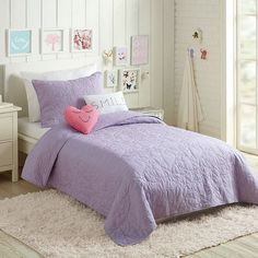 a bed with purple comforter and pillows in a white room next to a window