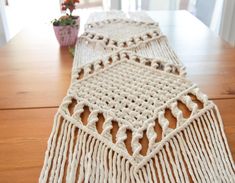 two crocheted table runners sitting on top of a wooden table next to a potted plant