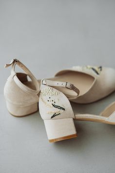 two pairs of shoes with embroidered flowers on the toes and heel, all in white