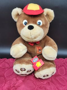 a brown teddy bear sitting on top of a pink table cloth with a red hat on it's head