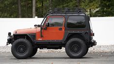 an orange and black jeep parked in front of a white fence