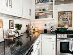 a kitchen with white cabinets and black counter tops is pictured in this image, there are pictures on the wall above the stove