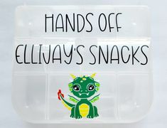 a clear plastic container with an image of a small green dragon on it and the words hands off ella's snacks