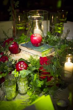 an apple sits on top of a book surrounded by greenery and candles