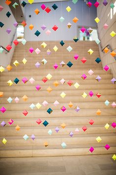 colorful paper cranes are hanging from the ceiling above some stairs in an office building with wooden steps