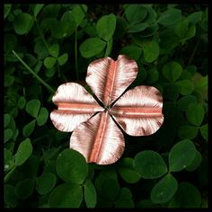 a four leaf clover is shown in the middle of some green leaves, and it appears to be made out of copper foil