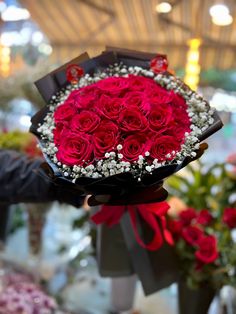 a bouquet of red roses is being held by someone's hand in a flower shop