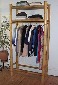 a bamboo rack with clothes hanging on it and a potted plant in the corner