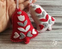 two red and white heart shaped ornaments hanging from string on wooden table with person's hand holding one