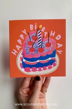 a hand holding an orange birthday card with a cake on it that says happy birthday